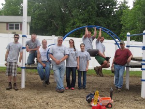 The United Way Day of Caring volunteers from Avery Dennison - James Baker, left to right,  Henry Milliman, Dave Berrow, Kyle Rhodes, Susan Rhodes, Frankie Masters, Ryan Lose, Josh  Bogner and Mike Webster - end their busy day at Forbes House by posing on the now weed- free playground many of them worked on once the rain stopped on June 25th. Some of the  team stayed inside shelter and finished their project in the playroom. Thanks volunteers for a job  well done!